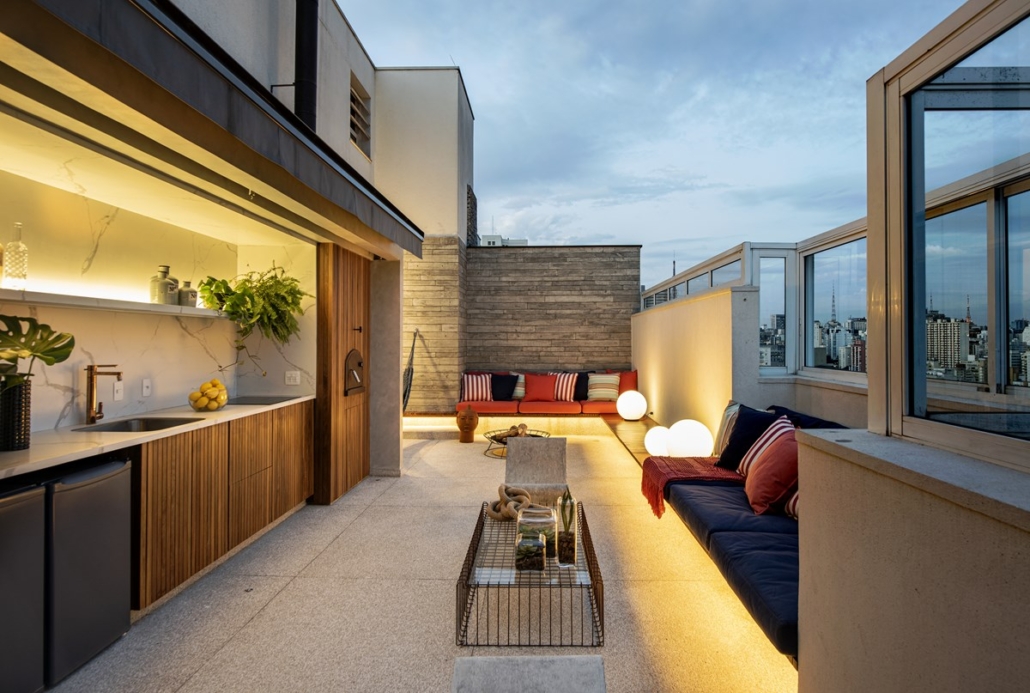 cobertura com sofá azul e vermelho com almofadas, mesa de centro e cadeiras. luzes acessas