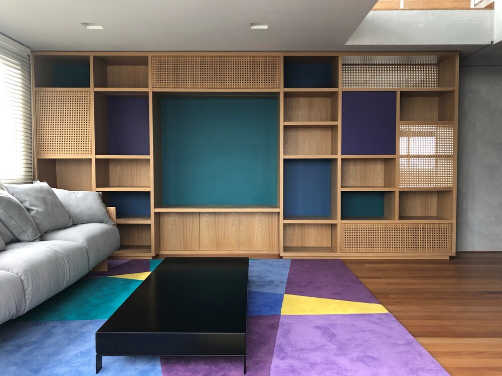 sala com sofá cinza e tapete colorido, estante grande na parede