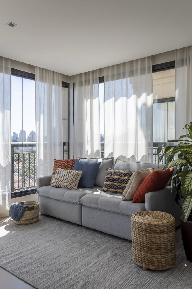 sala com sofá cinza e almofadas em cima, tapete cinza e decorações com plantas